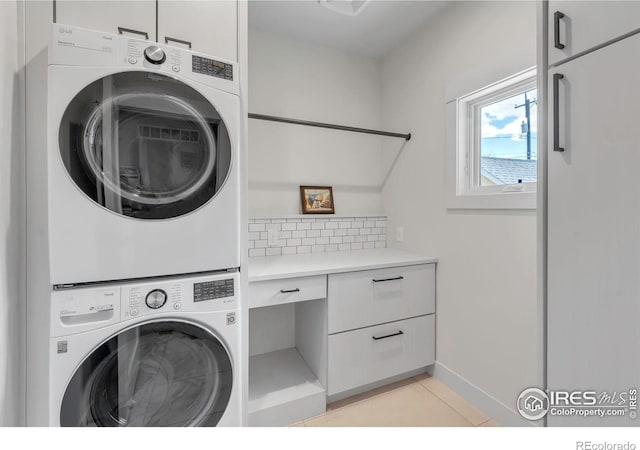 clothes washing area with stacked washer / dryer, cabinet space, light tile patterned floors, and baseboards