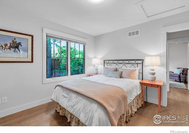 bedroom with baseboards, wood finished floors, and attic access