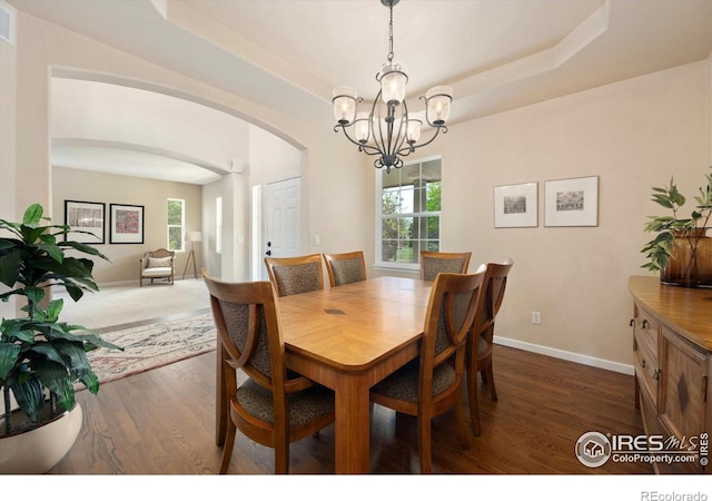 dining space featuring arched walkways, a chandelier, dark wood-type flooring, baseboards, and a tray ceiling
