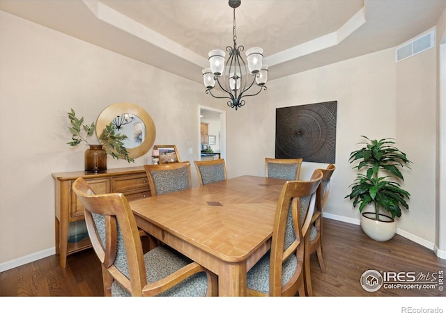 dining area featuring wood finished floors, baseboards, a chandelier, and a raised ceiling