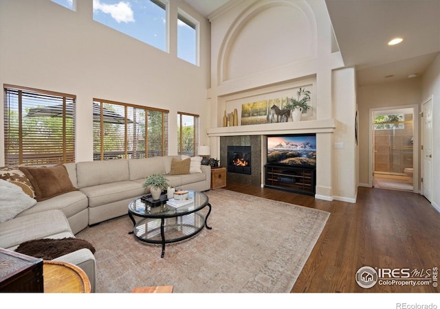living room featuring wood finished floors, a fireplace, baseboards, recessed lighting, and a towering ceiling