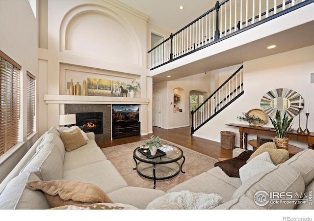 living room featuring stairs, a towering ceiling, arched walkways, wood finished floors, and a tile fireplace