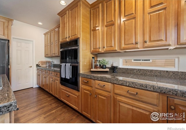 kitchen with tile counters, dark wood-style floors, recessed lighting, stainless steel fridge, and brown cabinets