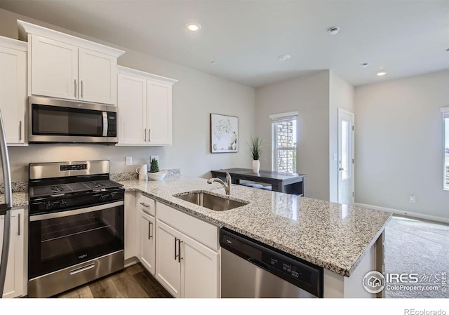 kitchen with stainless steel appliances, a sink, a peninsula, white cabinets, and light stone countertops
