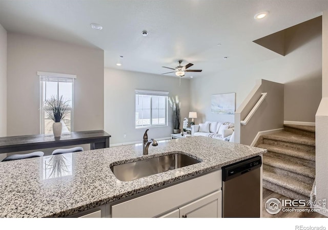kitchen with stainless steel dishwasher, a sink, white cabinets, light stone counters, and a ceiling fan