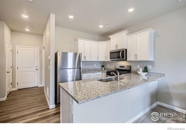kitchen with stainless steel appliances, a peninsula, a sink, baseboards, and white cabinetry