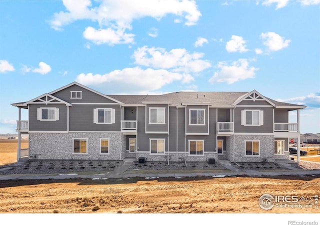 view of front of property with stone siding, a balcony, and central AC