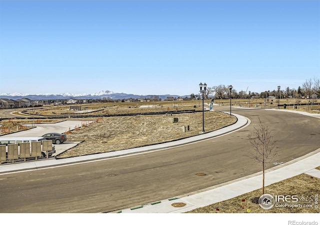 view of asphalt street with street lighting, a mountain view, curbs, and sidewalks