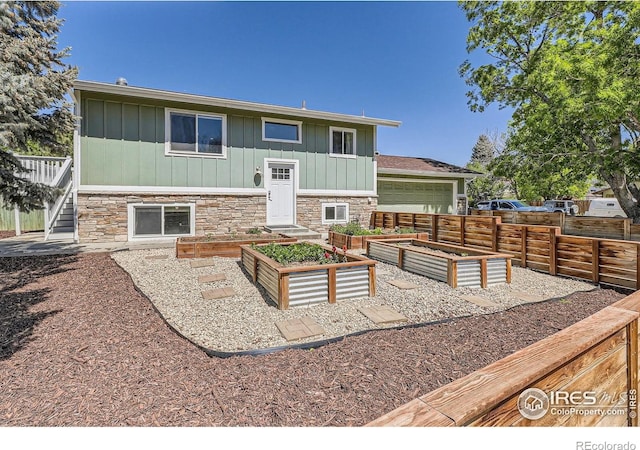 back of house featuring board and batten siding, a vegetable garden, stone siding, fence, and stairs