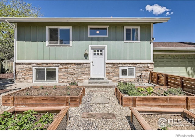 raised ranch featuring a vegetable garden, stone siding, and board and batten siding