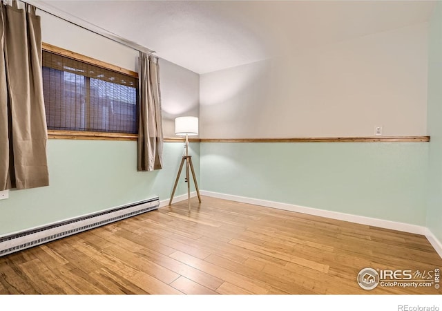 unfurnished room featuring a baseboard radiator, baseboards, and wood finished floors