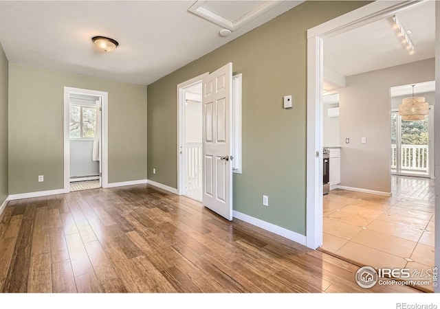 unfurnished bedroom featuring track lighting, wood finished floors, a baseboard radiator, baseboards, and an AC wall unit