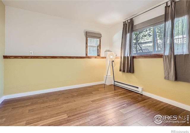 empty room featuring baseboard heating, plenty of natural light, wood finished floors, and baseboards