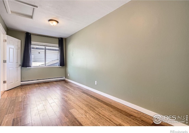 spare room with baseboard heating, attic access, wood finished floors, and baseboards