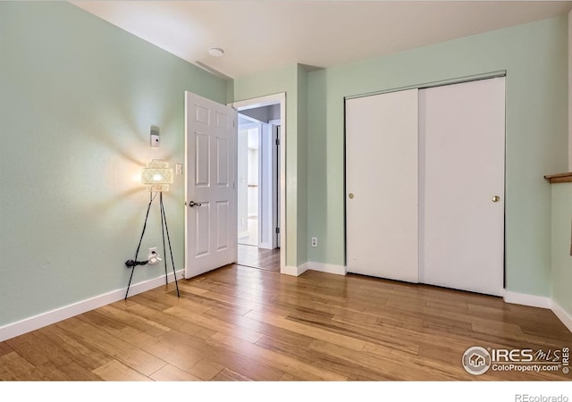 unfurnished bedroom featuring light wood-style flooring, baseboards, and a closet