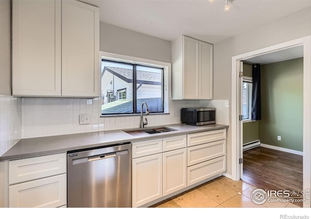kitchen featuring appliances with stainless steel finishes, a sink, baseboard heating, backsplash, and white cabinets