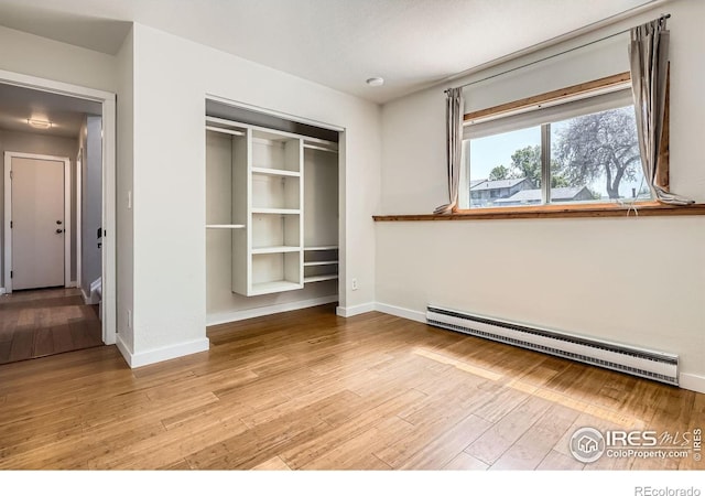 unfurnished bedroom featuring baseboard heating, light wood-style floors, a closet, and baseboards