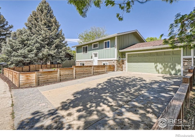 view of front of property with board and batten siding, concrete driveway, stone siding, a garage, and fence