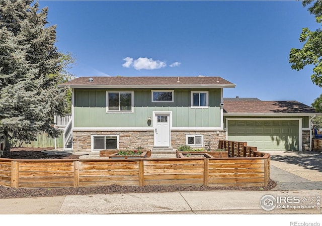 bi-level home featuring stone siding, a fenced front yard, driveway, and an attached garage
