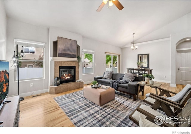 living area featuring lofted ceiling, wood finished floors, a tile fireplace, a ceiling fan, and baseboards