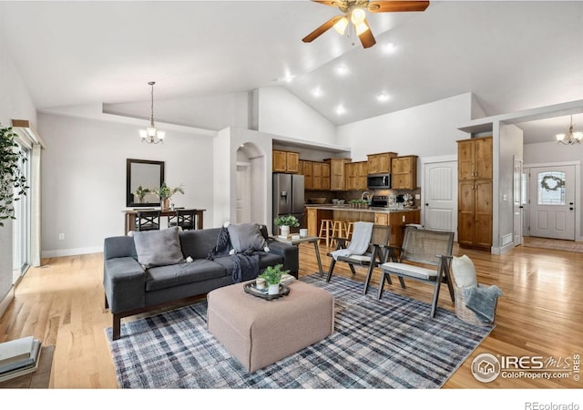 living area with a chandelier, light wood-type flooring, a ceiling fan, high vaulted ceiling, and arched walkways