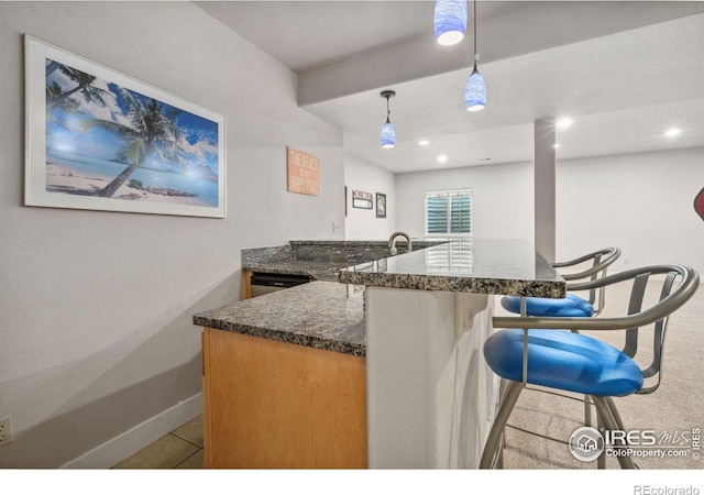 kitchen with dark stone countertops, baseboards, decorative light fixtures, a kitchen breakfast bar, and recessed lighting
