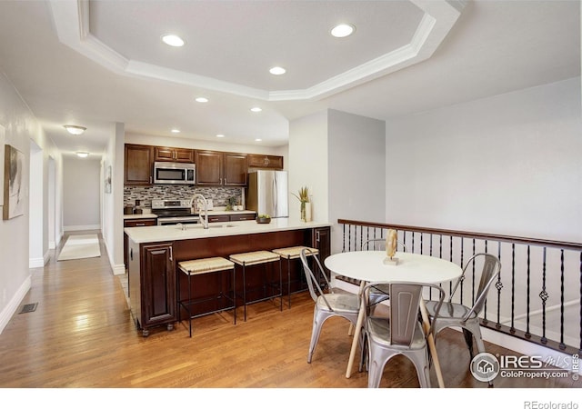 dining area featuring a raised ceiling, light wood finished floors, recessed lighting, baseboards, and crown molding