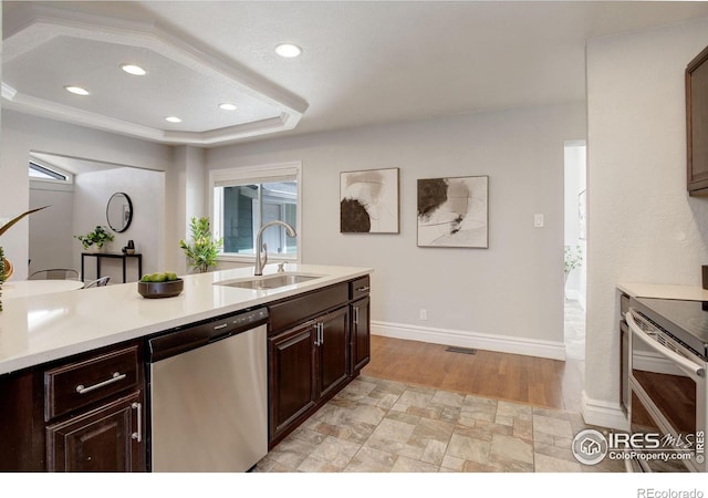 kitchen with stainless steel appliances, a sink, light countertops, dark brown cabinetry, and a raised ceiling