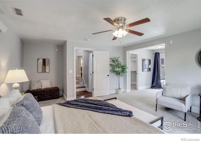 carpeted bedroom featuring a walk in closet, baseboards, and a ceiling fan