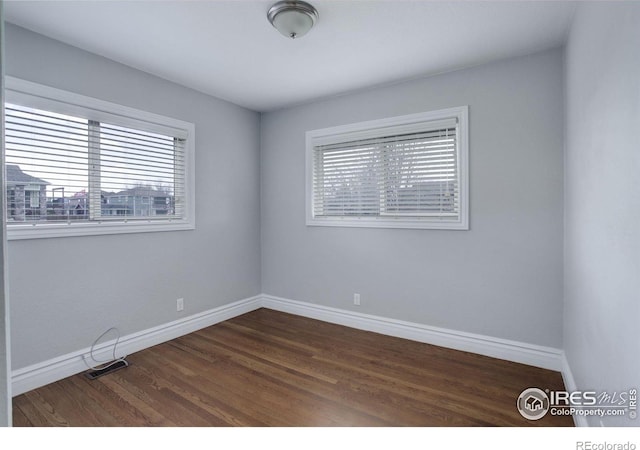 spare room with baseboards and dark wood-style floors