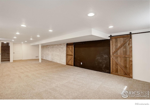 finished below grade area with carpet floors, a barn door, recessed lighting, and stairs