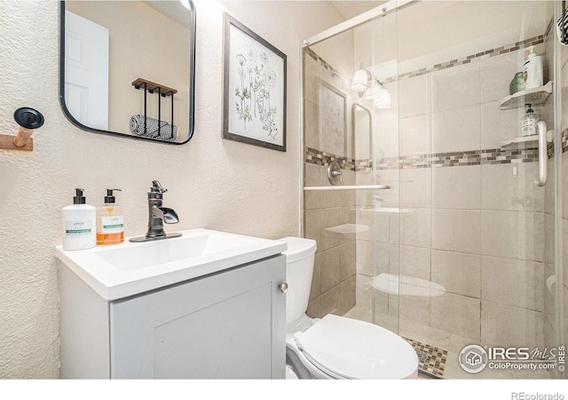 full bathroom with a textured wall, toilet, vanity, and a shower stall