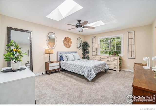 carpeted bedroom with a skylight, baseboards, and ceiling fan