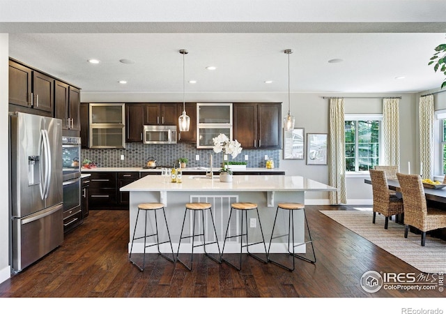 16069 Pikes Peak Dr, Broomfield, CO 80023 - kitchen with appliances with stainless steel finishes, light countertops, a breakfast bar, dark wood-type flooring, and dark brown cabinetry