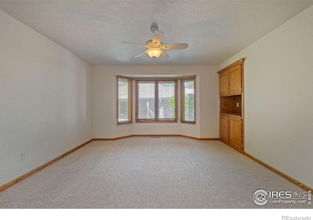 spare room featuring light carpet, a ceiling fan, baseboards, and a textured ceiling