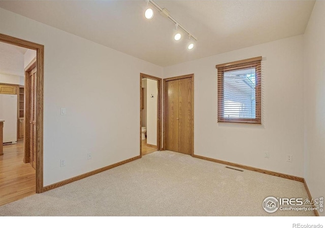 unfurnished room featuring light colored carpet, baseboards, and track lighting