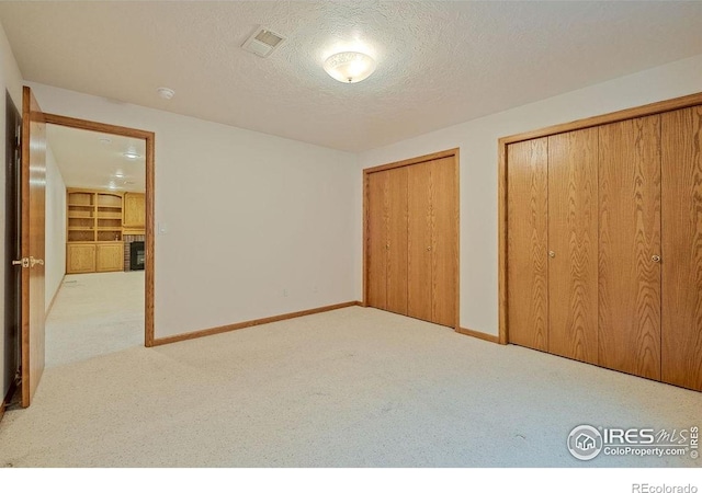 unfurnished bedroom featuring carpet floors, multiple closets, a textured ceiling, and baseboards