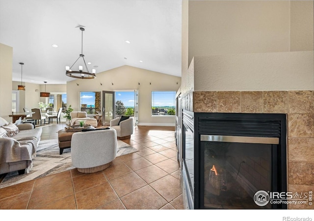 living area with a tile fireplace, healthy amount of natural light, vaulted ceiling, tile patterned flooring, and a chandelier