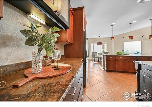 kitchen with brown cabinetry, decorative light fixtures, light tile patterned floors, dark stone counters, and recessed lighting