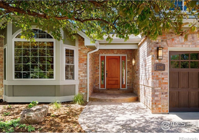 entrance to property featuring an attached garage and brick siding