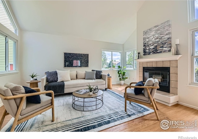 living area with wood finished floors, a tiled fireplace, baseboards, and high vaulted ceiling