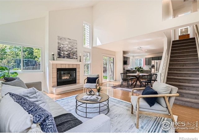 living room with stairs, high vaulted ceiling, light wood-style floors, and a tile fireplace