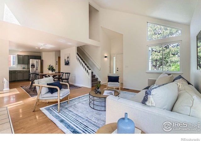 living area featuring stairway, high vaulted ceiling, light wood-style floors, and healthy amount of natural light