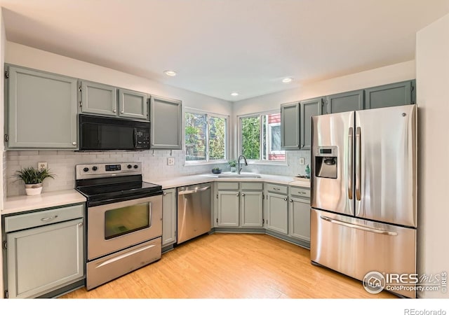 kitchen with stainless steel appliances, light countertops, backsplash, light wood-type flooring, and a sink
