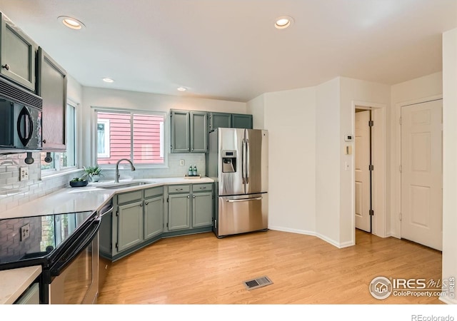 kitchen featuring stainless steel fridge with ice dispenser, a sink, electric range, black microwave, and light wood-type flooring