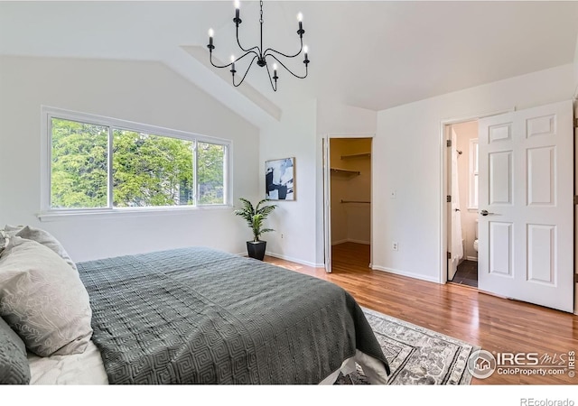 bedroom featuring a chandelier, wood finished floors, a spacious closet, vaulted ceiling, and baseboards