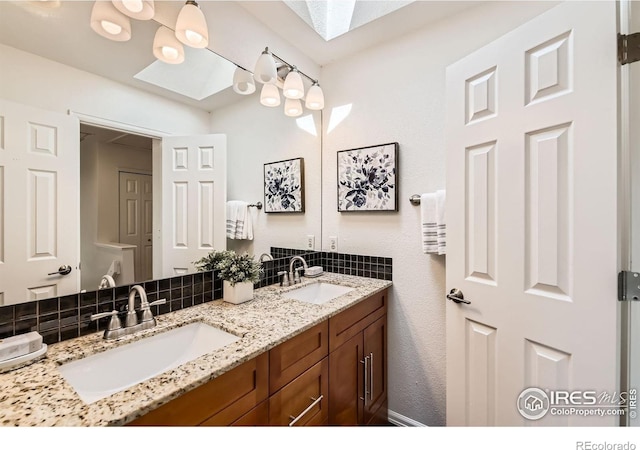 full bath with a skylight, double vanity, and backsplash