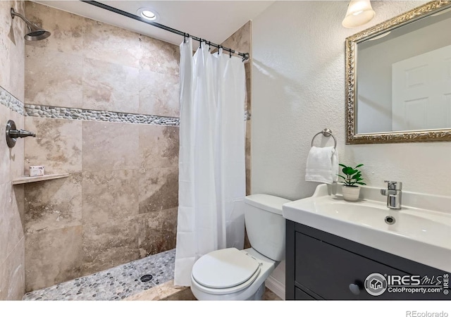 bathroom with toilet, a tile shower, vanity, and a textured wall