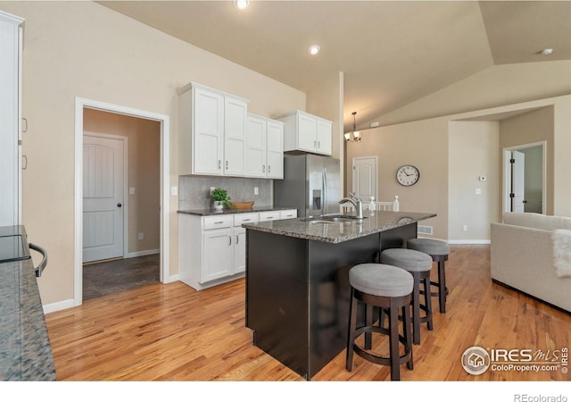 3933 Mount Hope St, Wellington, CO 80549 - kitchen featuring stainless steel refrigerator with ice dispenser, a sink, light wood-type flooring, a breakfast bar area, and lofted ceiling