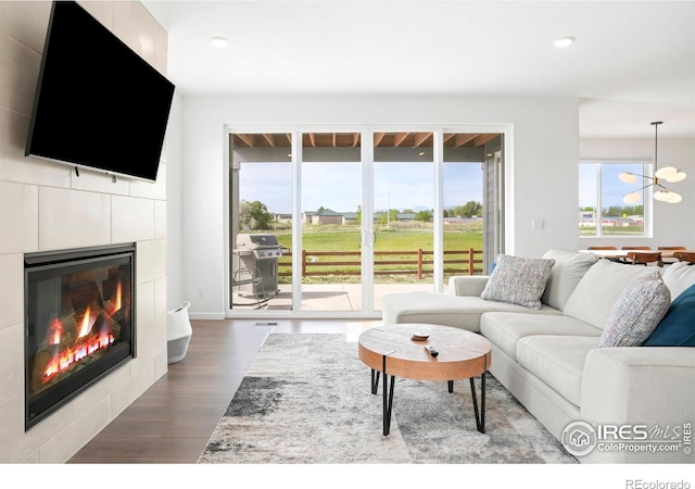 living area with plenty of natural light, dark wood-type flooring, a tiled fireplace, recessed lighting, and a chandelier